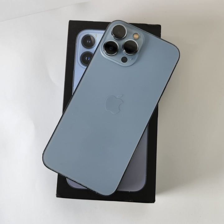 An Apple iPhone 13 Pro Max in Sierra Blue with a new case and screen protector, displayed in front of its packaging box.