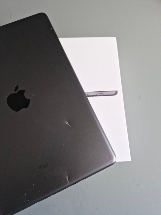 Apple iPad 7 32GB Wifi Space Grey - New Battery (Imperfect) Black Apple laptop on a gray surface with a white paper underneath