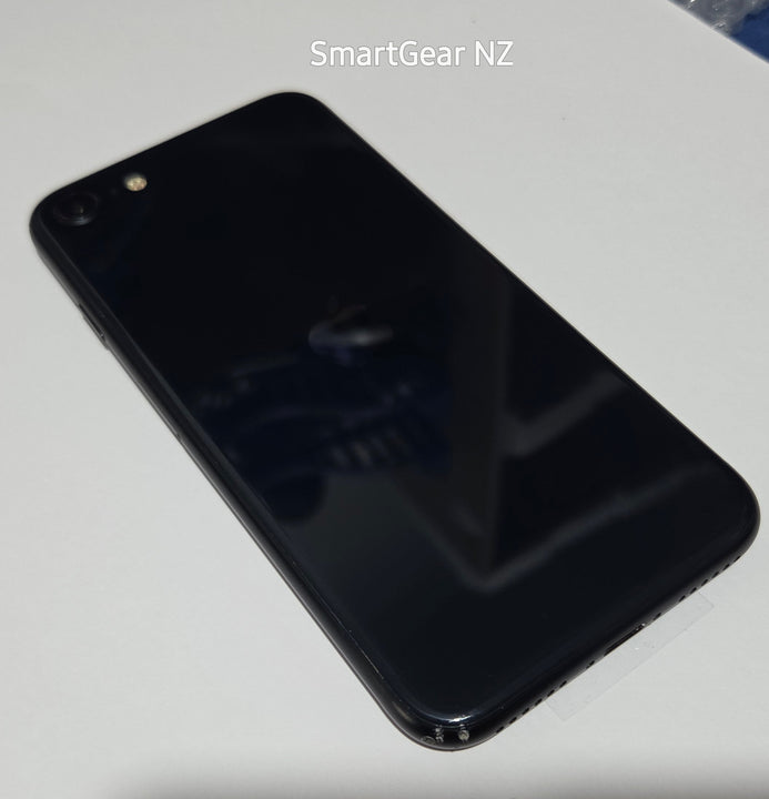 A black smartphone shown from the back, resting on a white surface with blue fabric visible around the edges. A faint 'SmartGear NZ' watermark appears near the top.